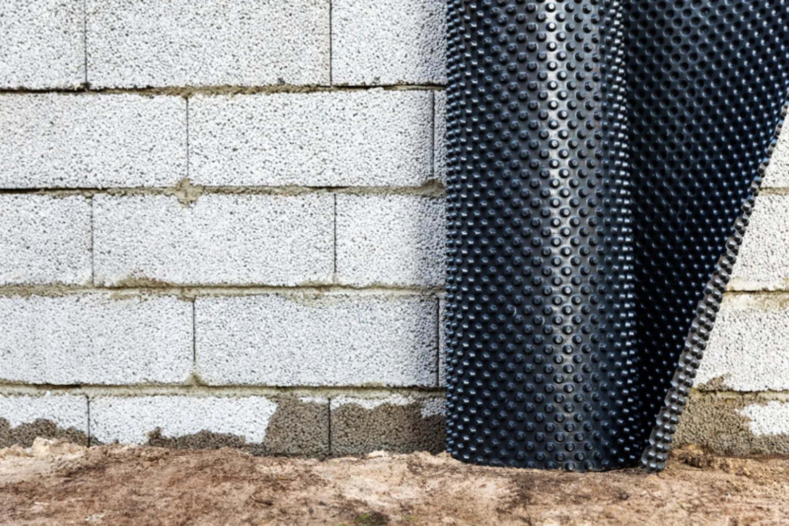 Sort knopmembran rulles ud mod en kældervæg af letbetonblokke